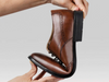 Anatomic & Co Fata - laced Brown leather formal shoe held and bent to display flexibility against a grey background. 
