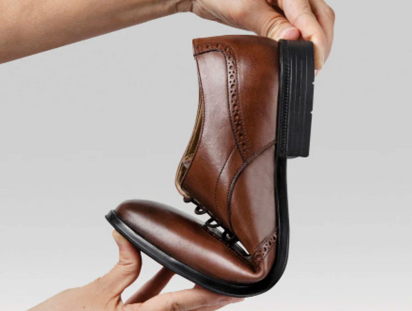 Anatomic & Co Fata - laced Brown leather formal shoe held and bent to display flexibility against a grey background. 