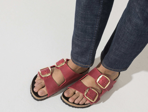 Birkenstock Arizona Big Buckle 1020163 - Fire Red double strap sandal with large gold buckles and a cork footbed with a black sole worn with dark blue jeans on a white background