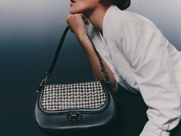 Person holding Hispanitas BI254150 Hand Bag - Black / White with houndstooth pattern and black leather sides on a dark background