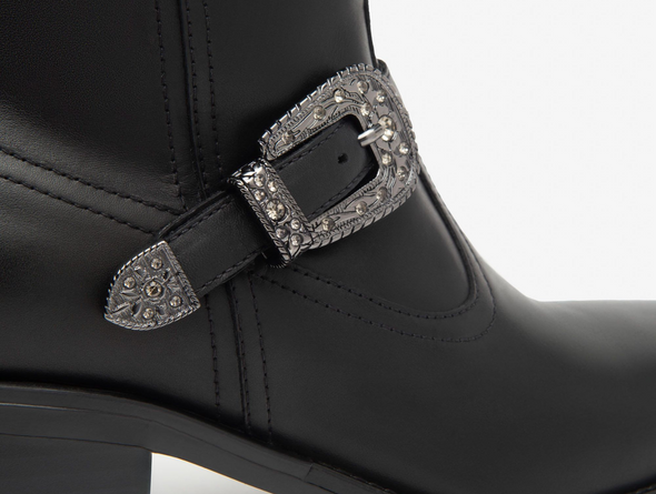 Close up of NeroGiardini I513900D 100 - Black western inspired ankle boots with a silver buckle on a white background 