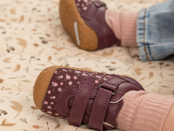 Close-up of a baby wearing Startrite Little Smile 0823-18 - Burgundy floral baby shoes with Velcro straps and a rubber sole on a soft surface