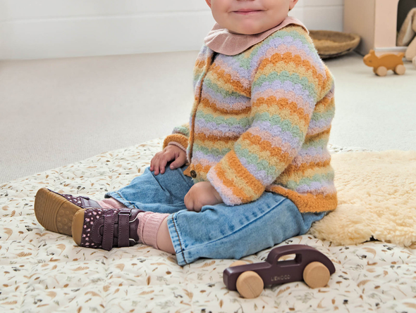 Child wearing a colorful striped sweater sitting on a carpeted floor with toys around wearing Startrite Little Smile 0823-18 - Burgundy floral baby shoe with Velcro straps and a rubber soles